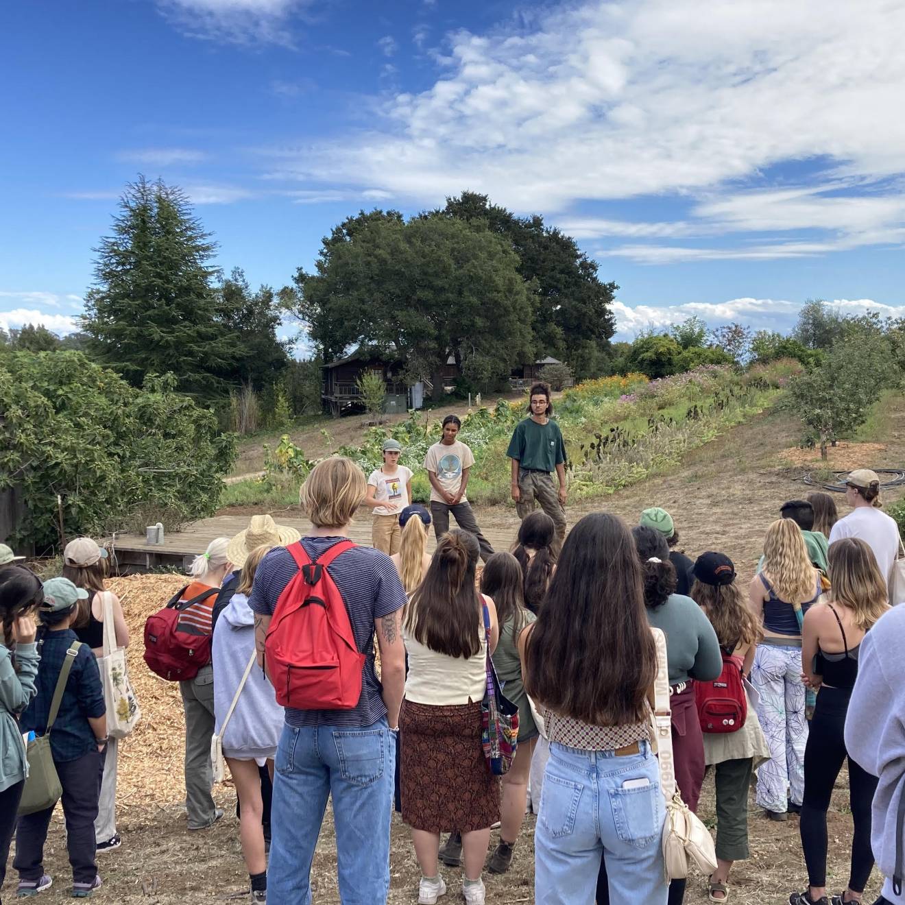 Two people speak to a small crowd of students in a garden