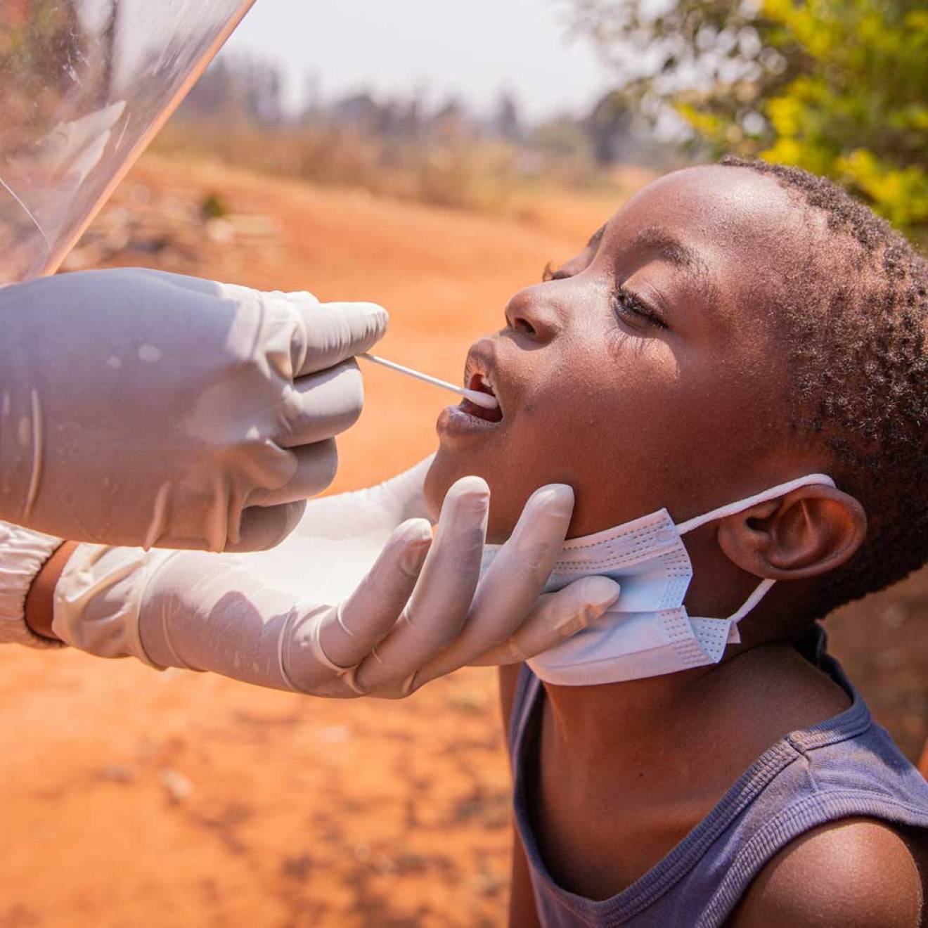 A young African child gets a tongue swab test from a medical professional.