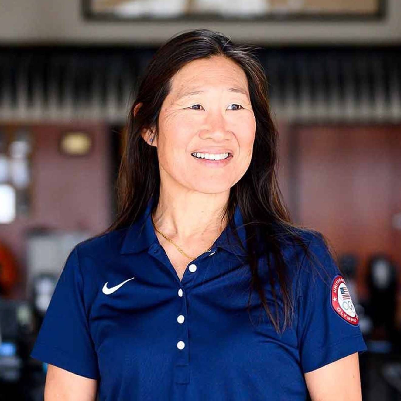 Dr. Cindy Chang poses for a portrait in front of a set of exercise equipment. In the background is a framed Olympic flag.