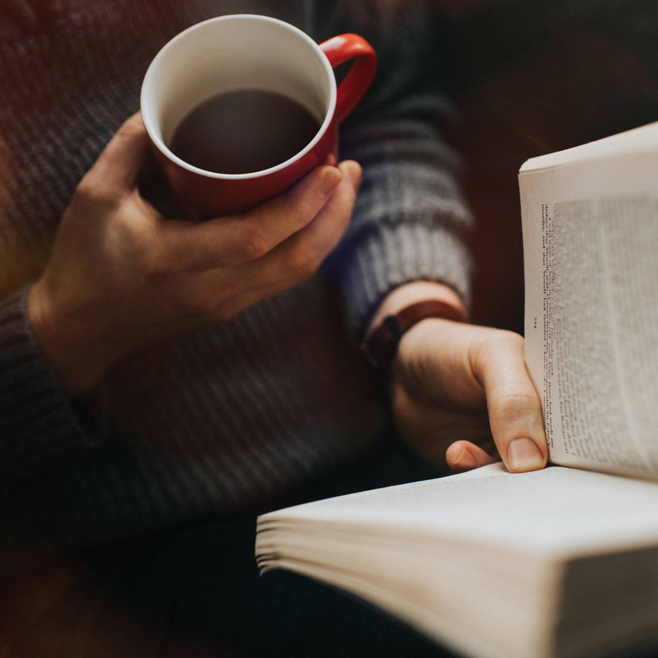 A view of someone holding a cup of coffee and reading a book from above