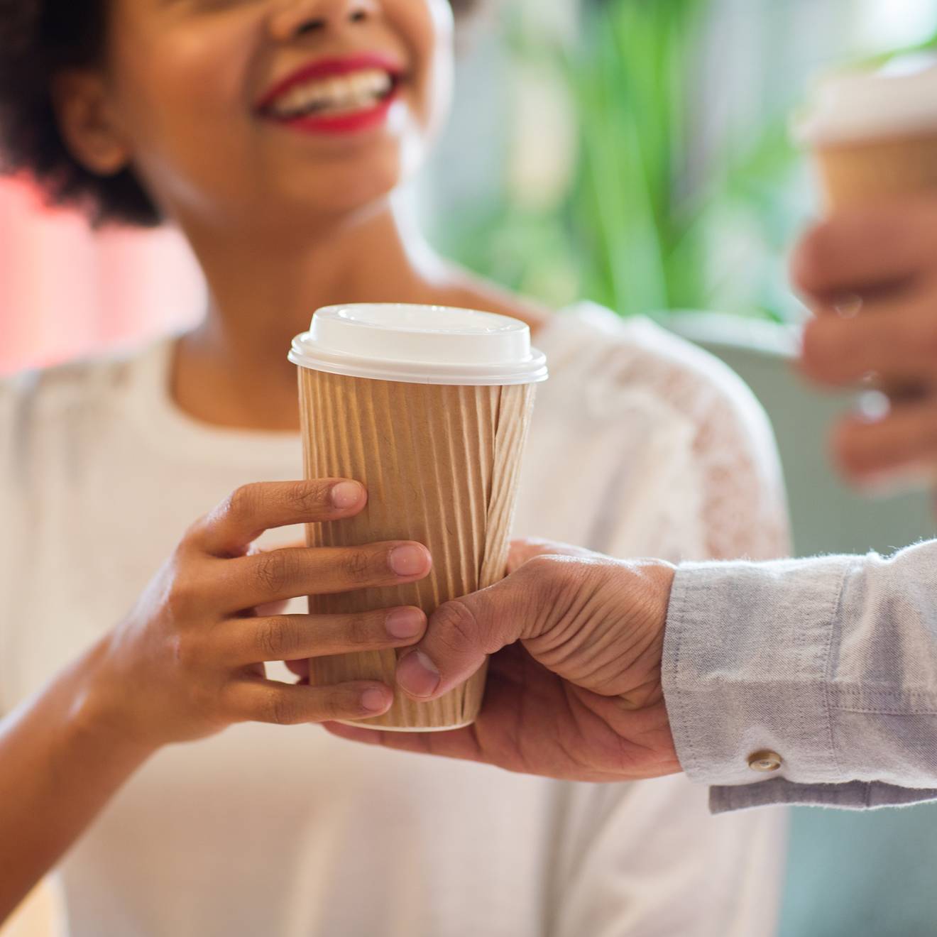 A person hands a smiling Black woman a to go cup of coffee