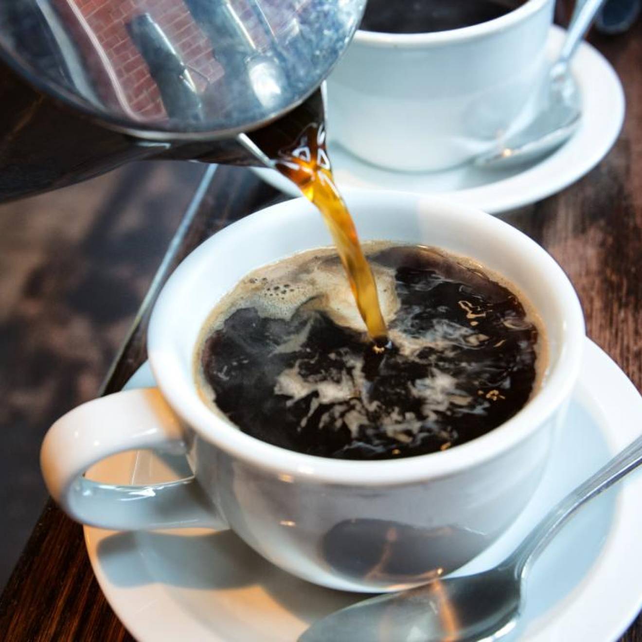 Coffee being poured into a cup, another cup behind it