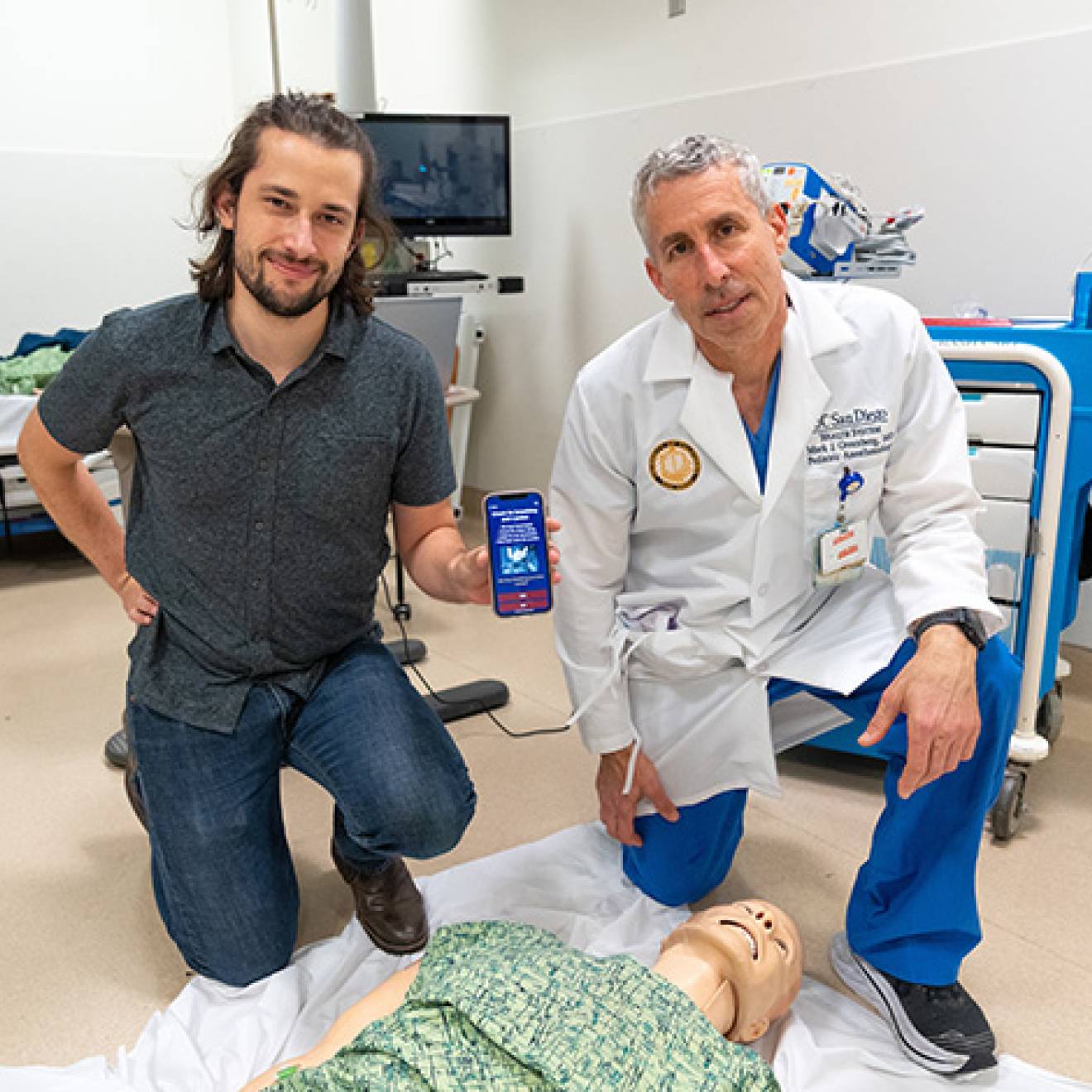 Medical student and a doctor kneeling over a CPR dummy with the app