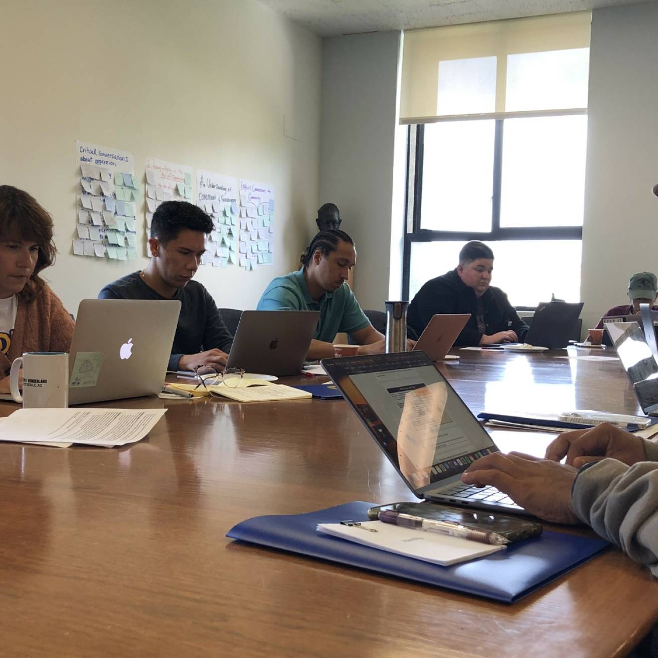 A diverse group of teachers working on laptops together on a wooden table