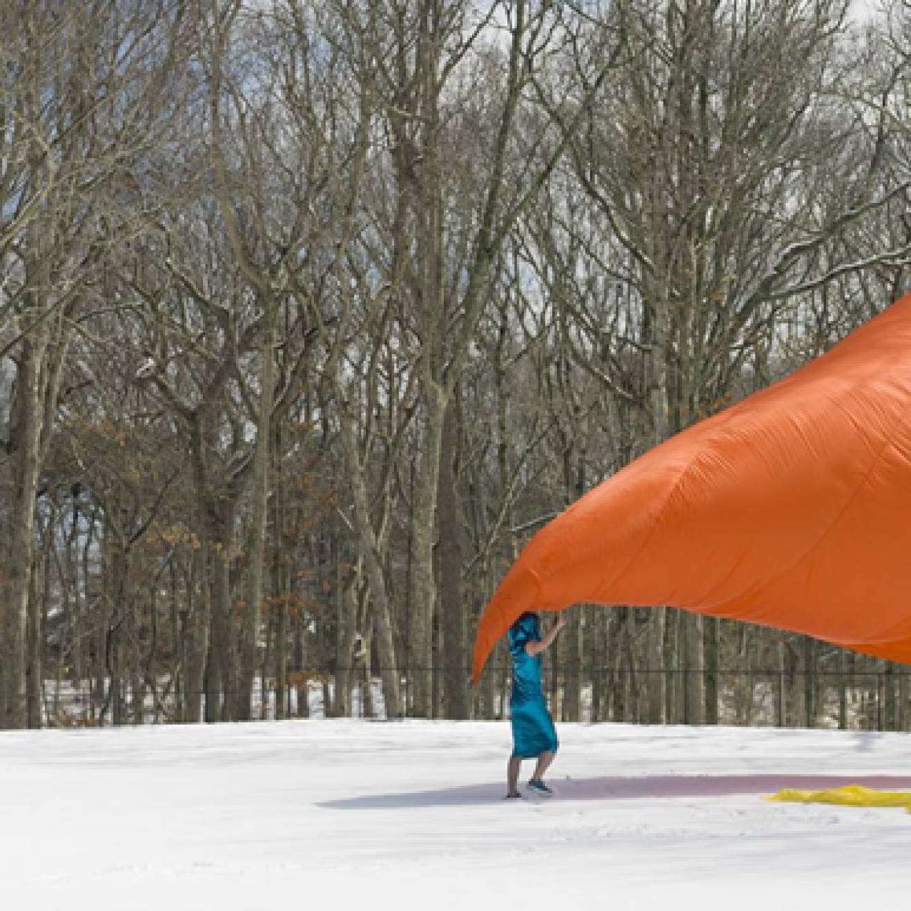 Three people performing with a giant orange sheet outside in the snow