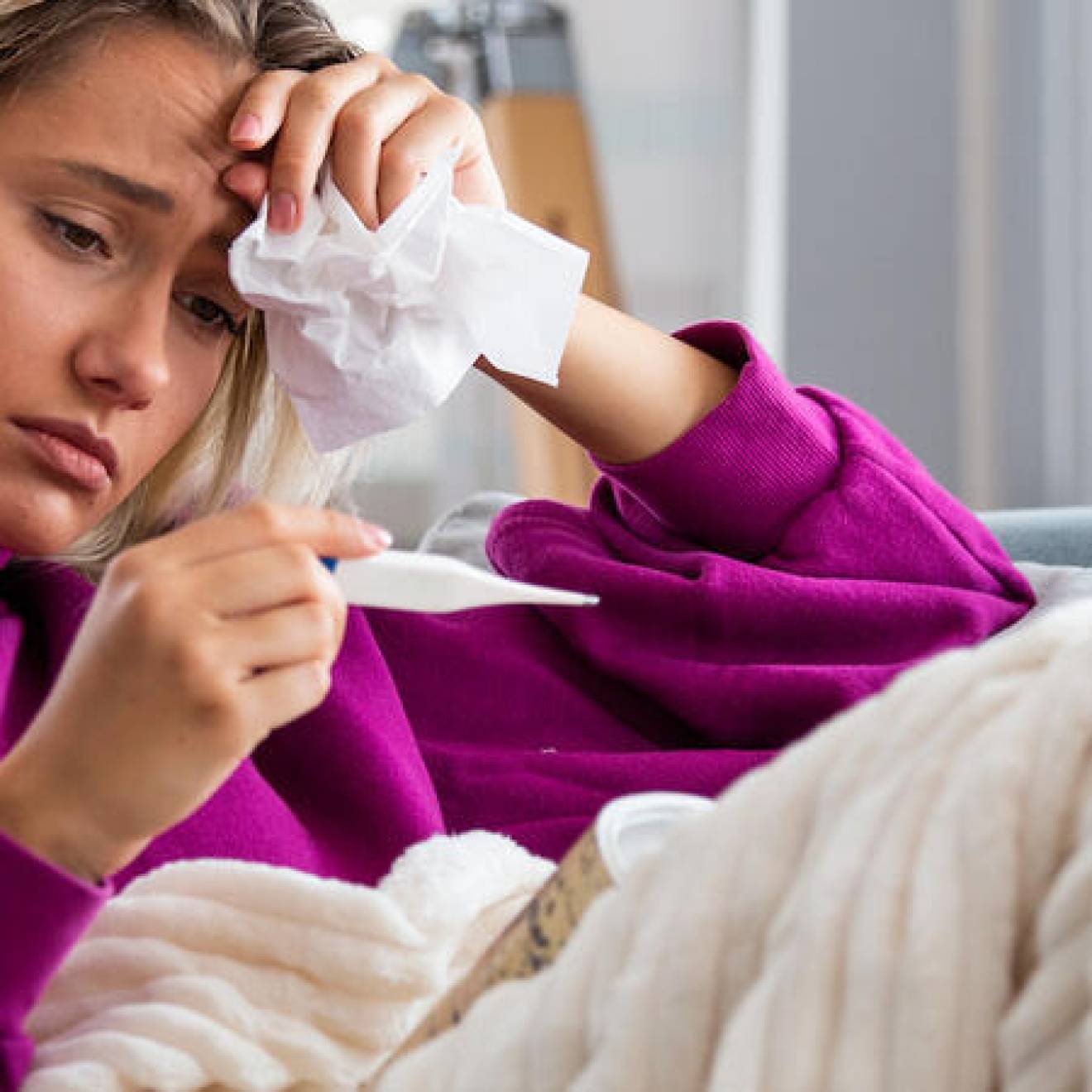Woman sitting on a couch looking a thermometer
