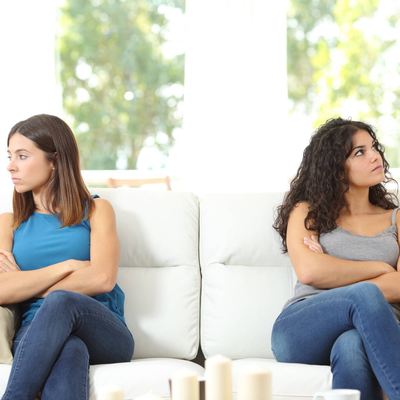 Young women on a couch looking away from each other, arms crossed
