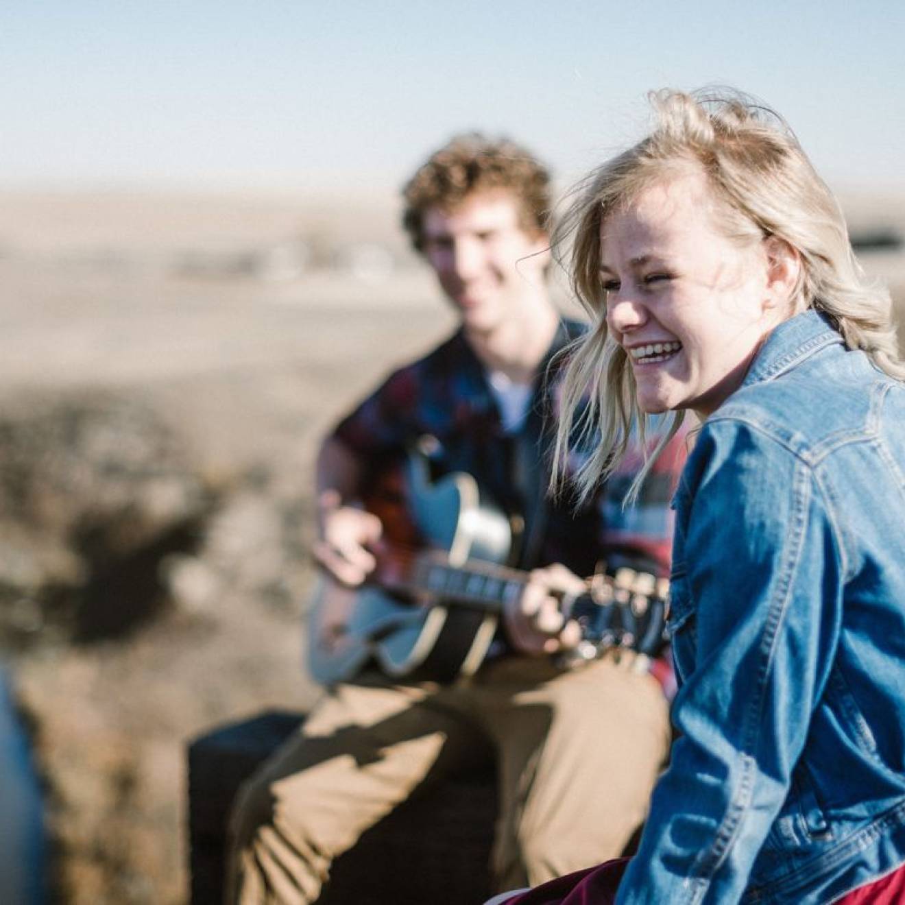 A happy woman smiling as she listens to a man play guitar