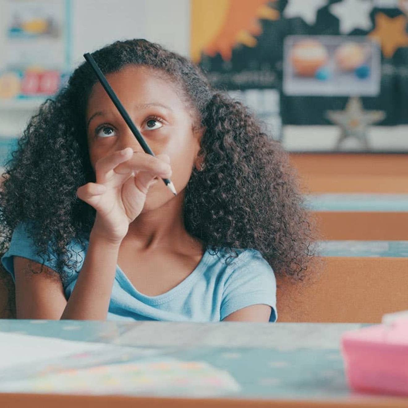 Young Black girl in classroom playing with her pencil, bored