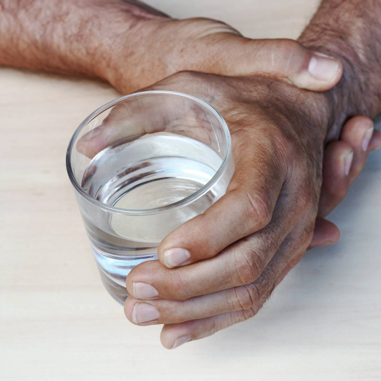 A man steadying a hand holding a glass of water with his other hand