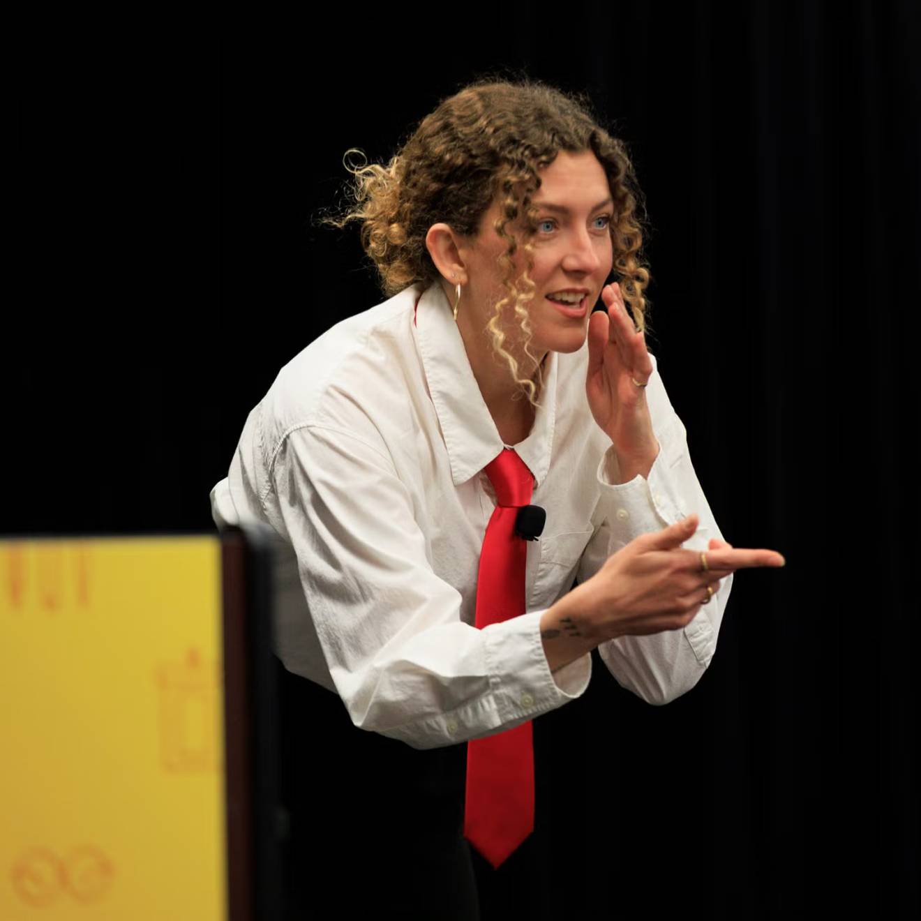 A woman in a white blouse and red tie makes a chopping gesture while pointing during a presentation