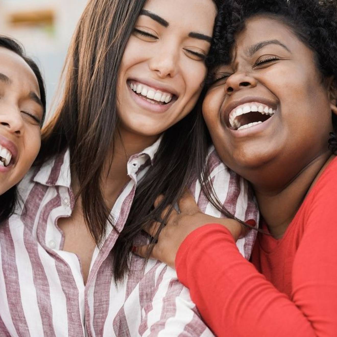 Three women laugh while in a group hug