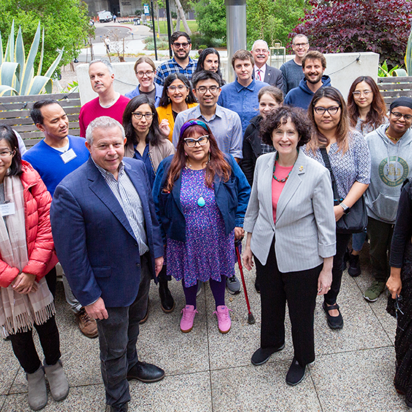 A group of people stand on a patio with lots of plants smiling for a group photo