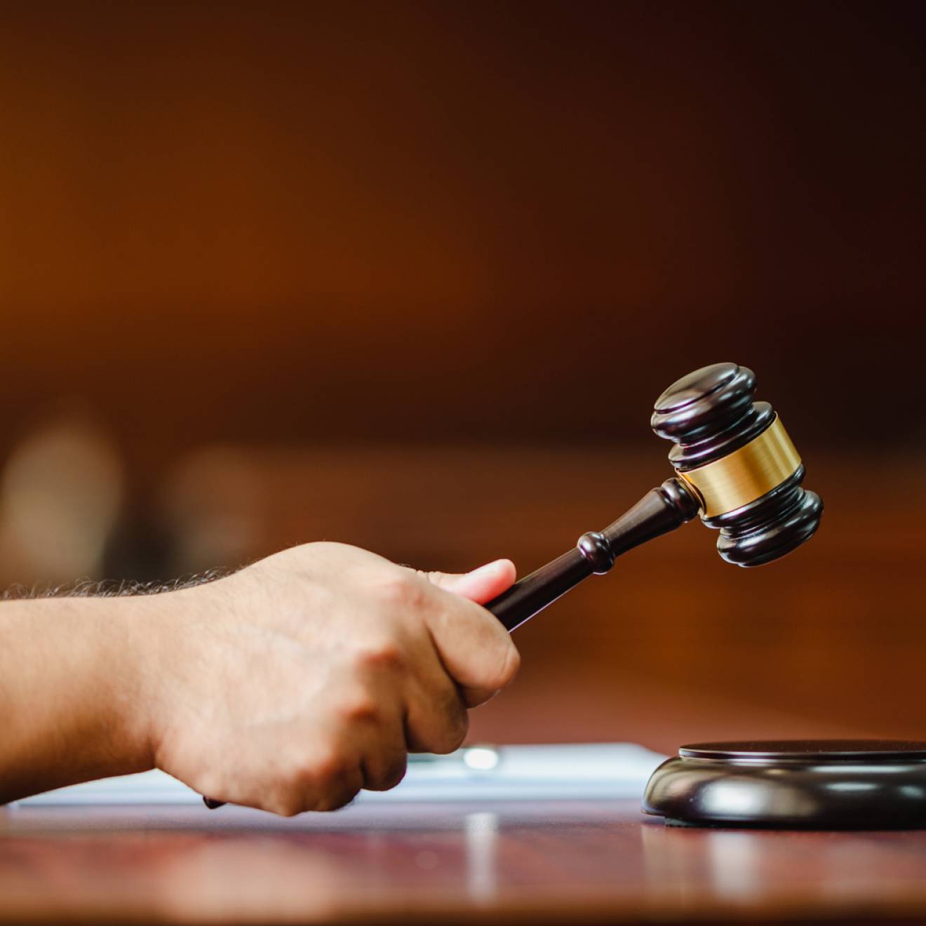 Closeup hand of a woman Judge with gavel at wooden table indoors at the courtroom