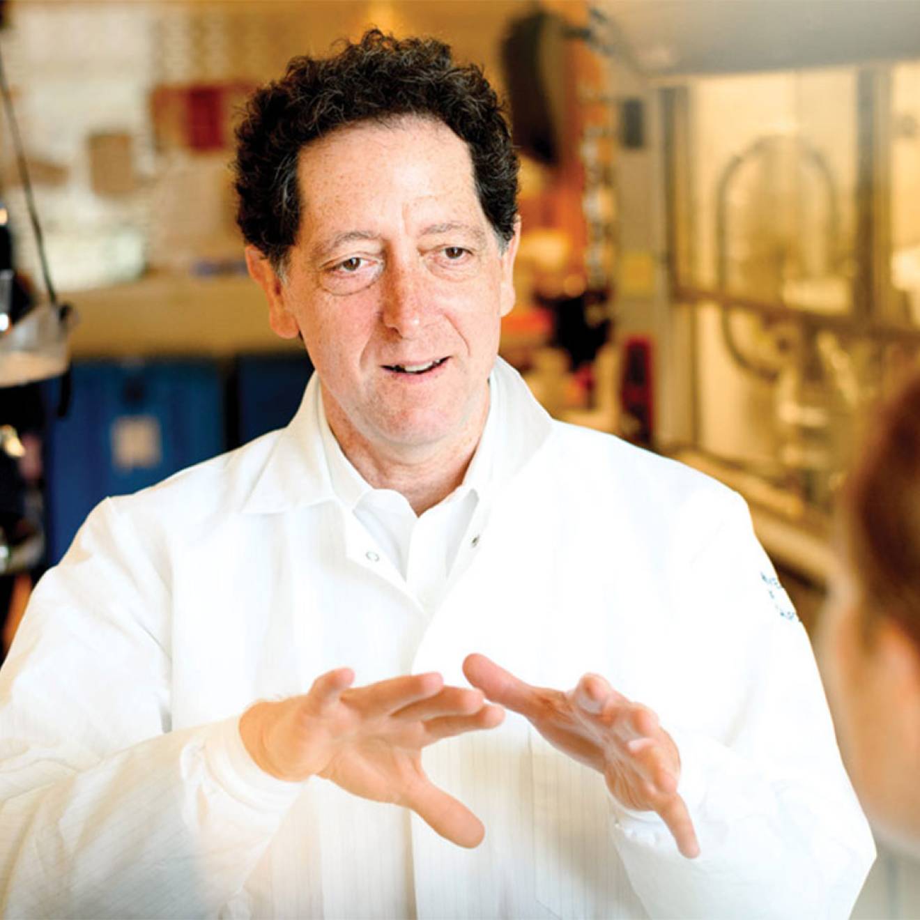 Kevan Shokat in a white lab coat speaking to a grad student in a lab.