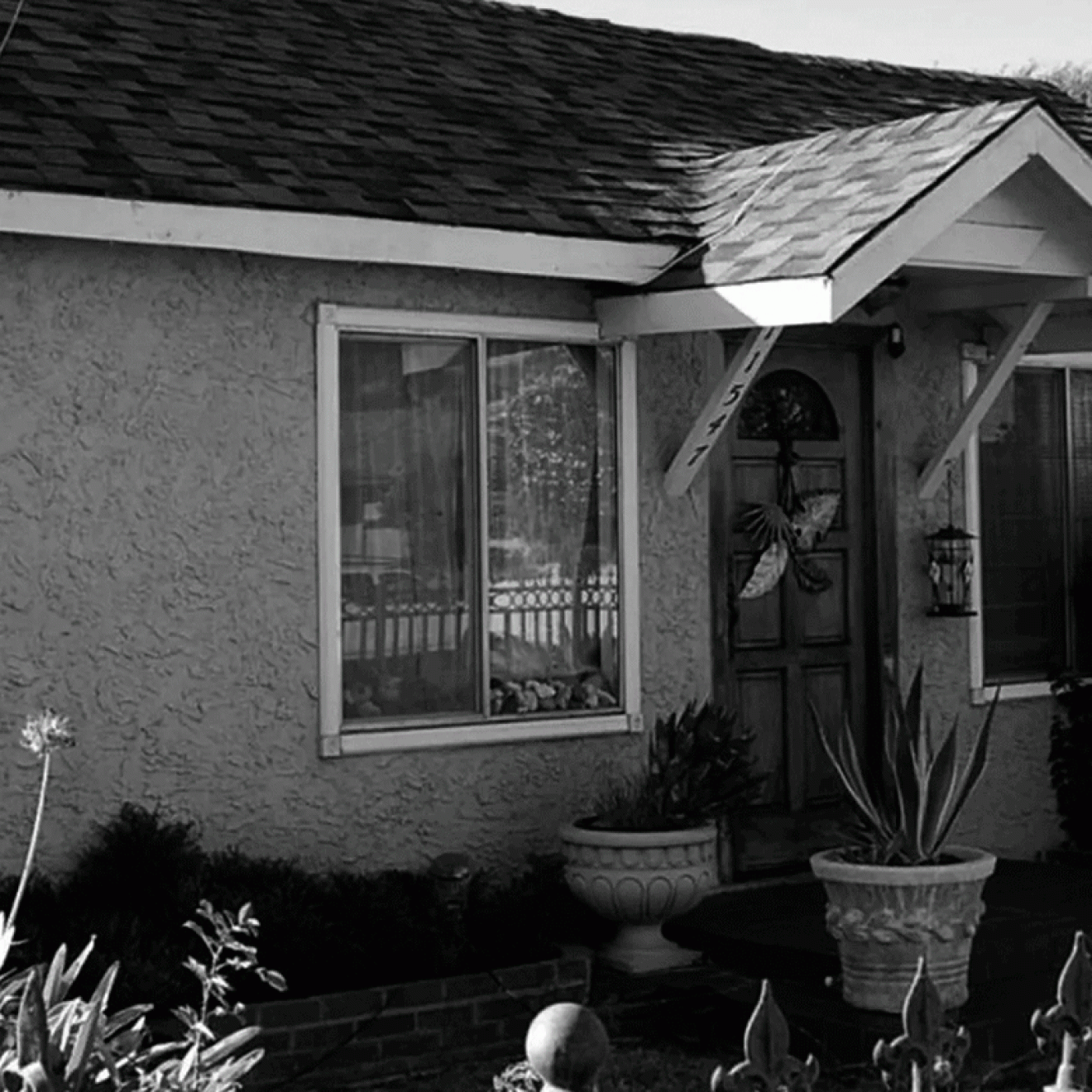 Black and white photo of a modest stucco house with eerie green lights flashing in the window