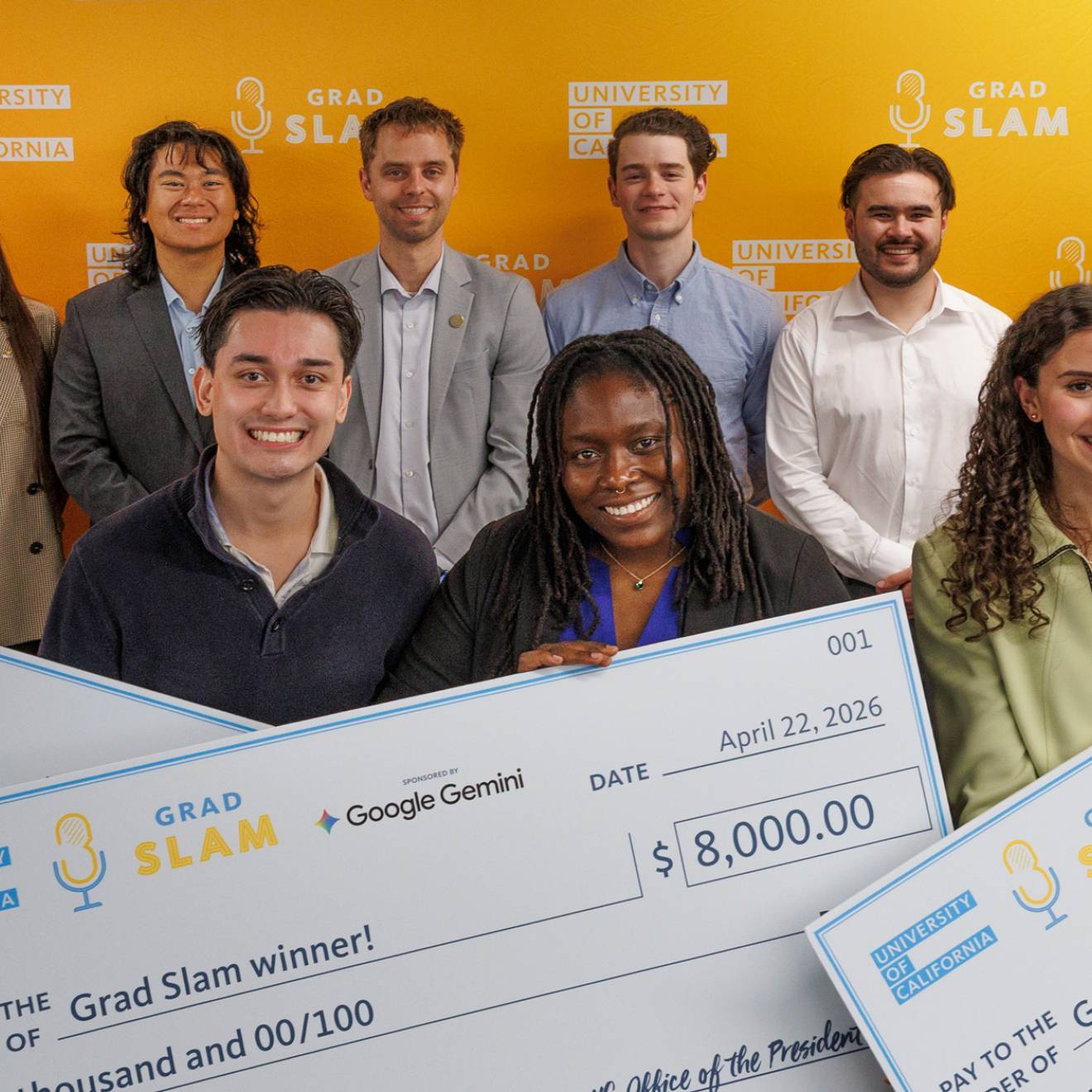 A group of smiling students, three of them holding giant prize money checks