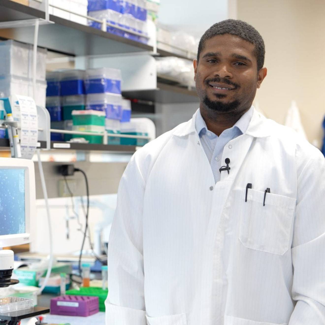 Young Black man with a goatee in a lab coat in a lab, smiling