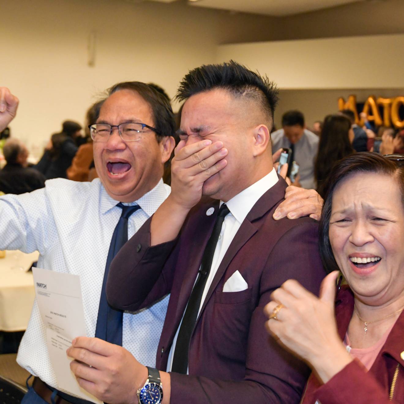 A UC Riverside medical student holds his hand over his mouth in excitement, flanked by his parents, on Match Day