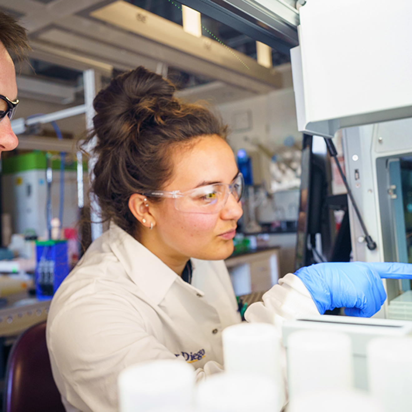 A man and a woman pointing at a machine in a lab