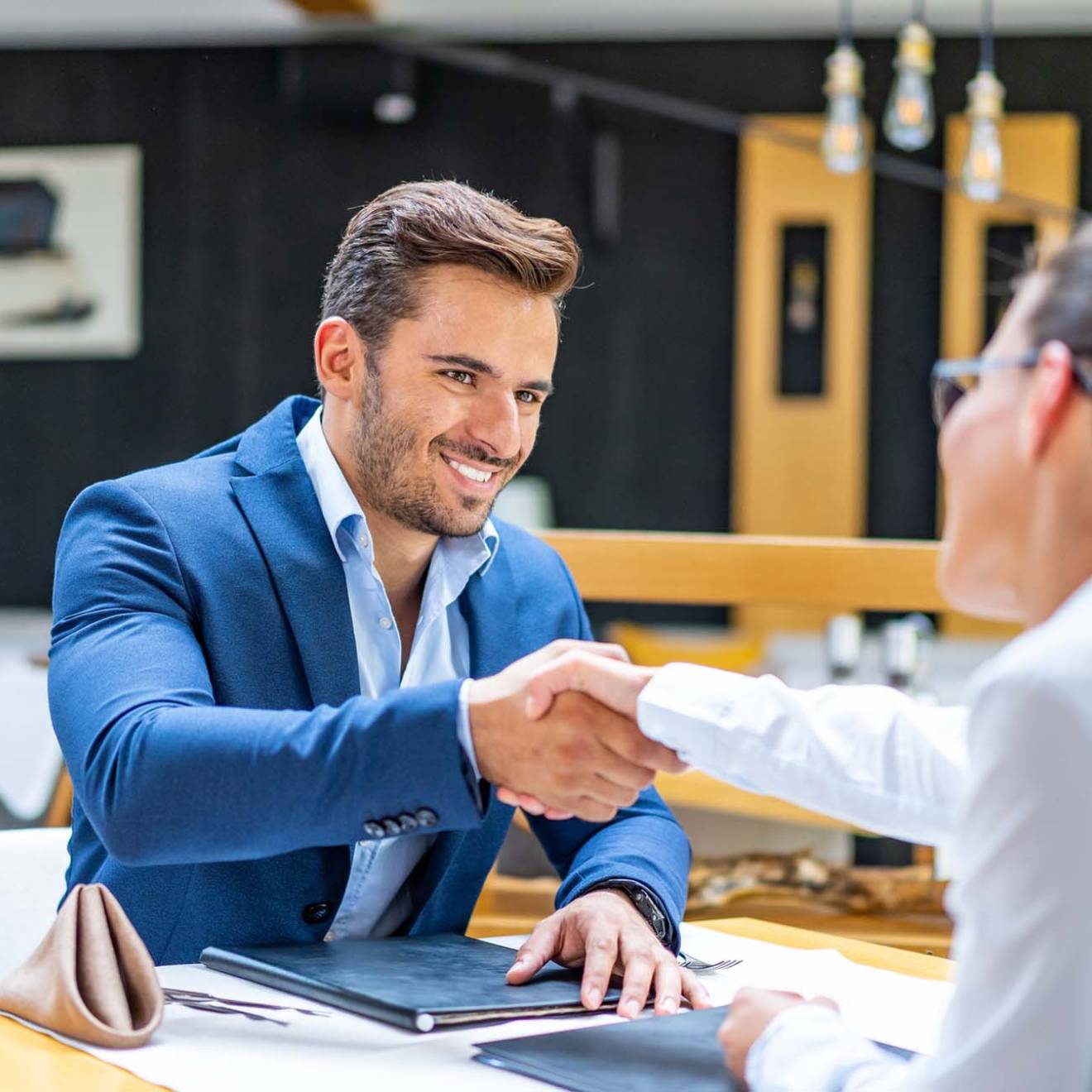 Man smiling and shaking the hand of a woman over a table