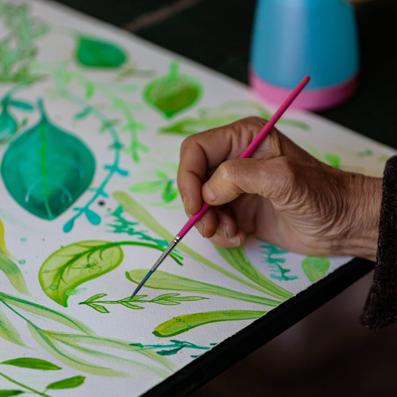 An older adult painting, hand on leaf decorative painting pictured