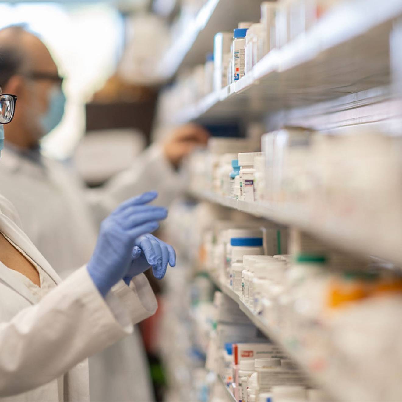 A pharmacist in a face mask reaching for drugs