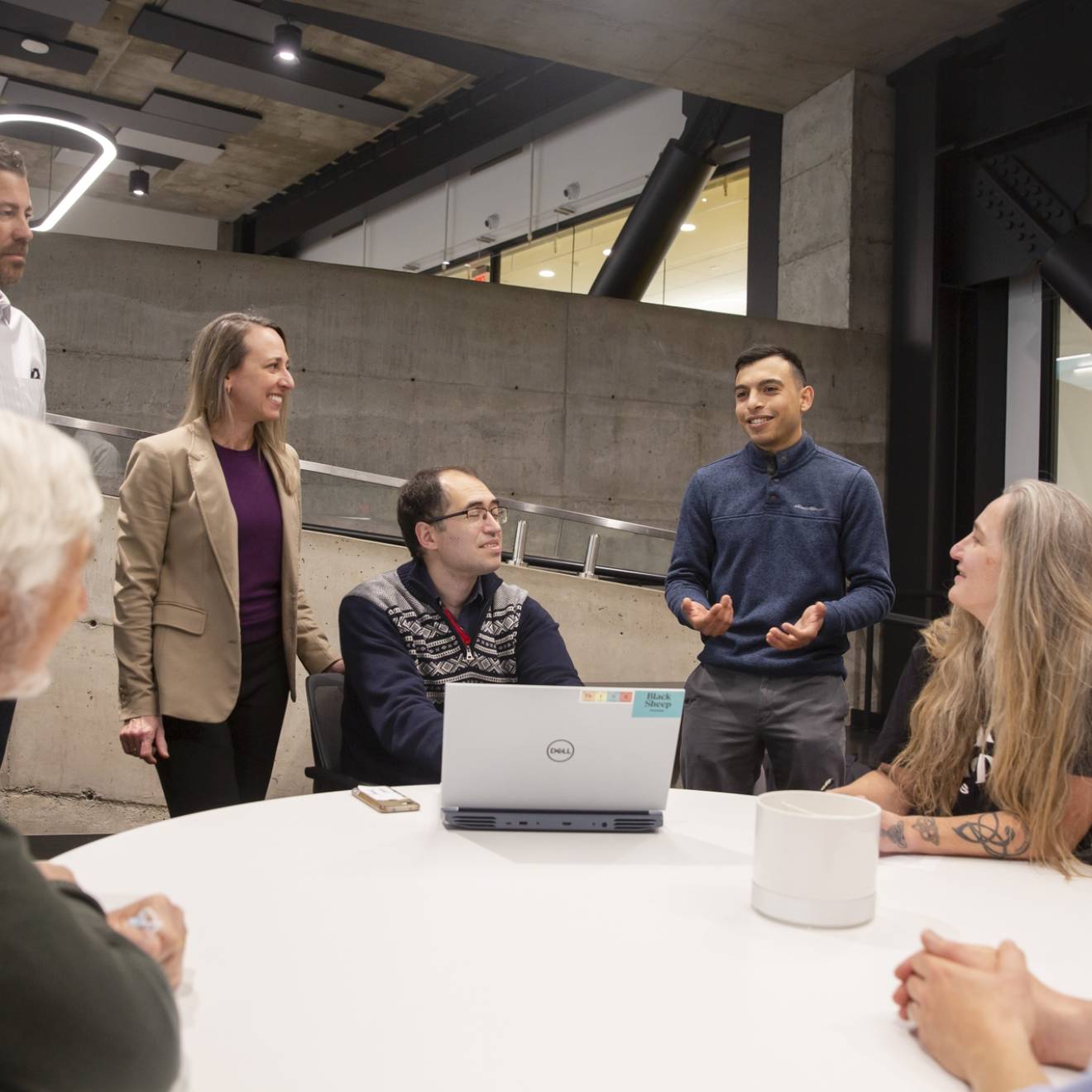 A group of people discussing, a few standing, while in an industrial or modern office space