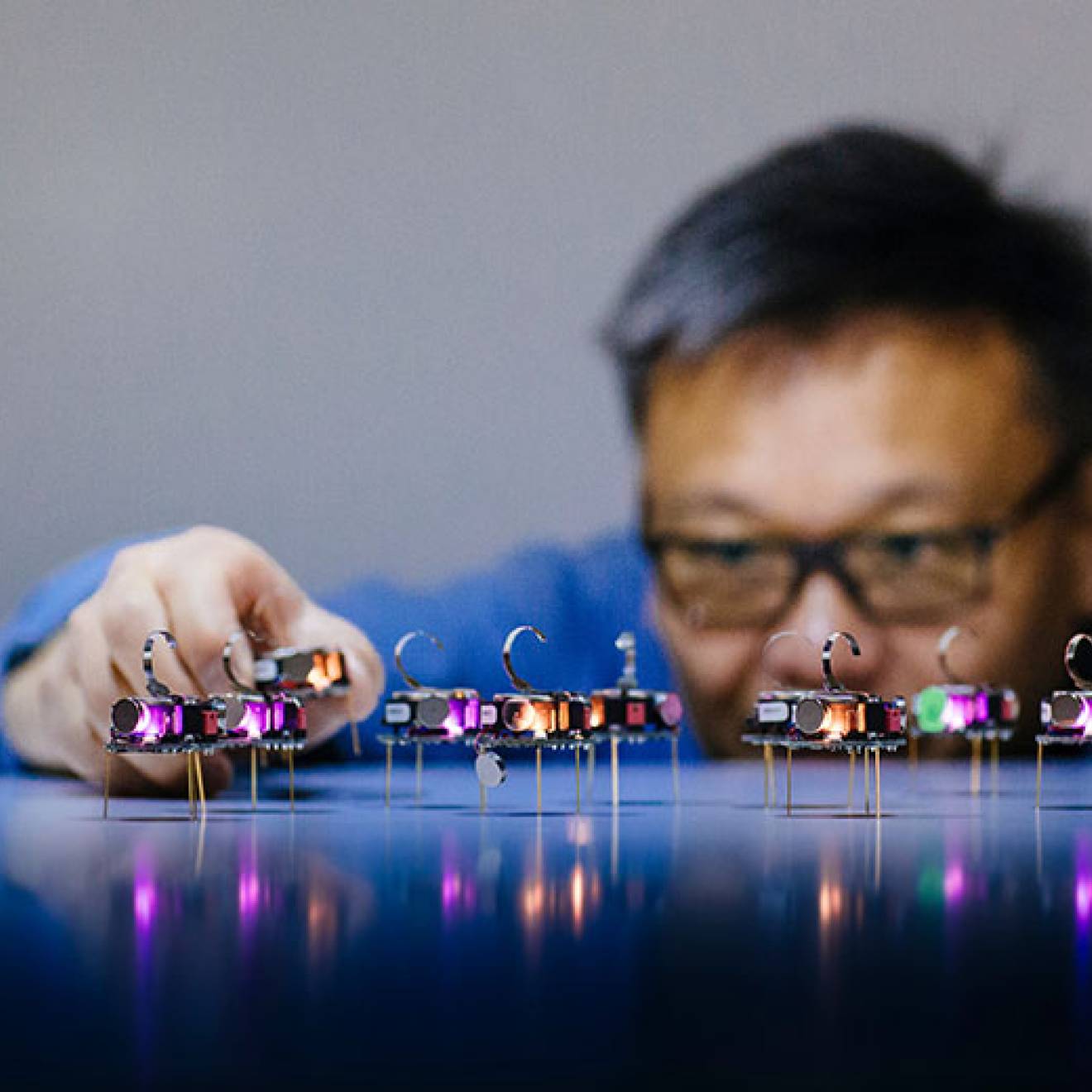 A researcher adjusts a row of small illuminated electronic devices on a reflective surface.