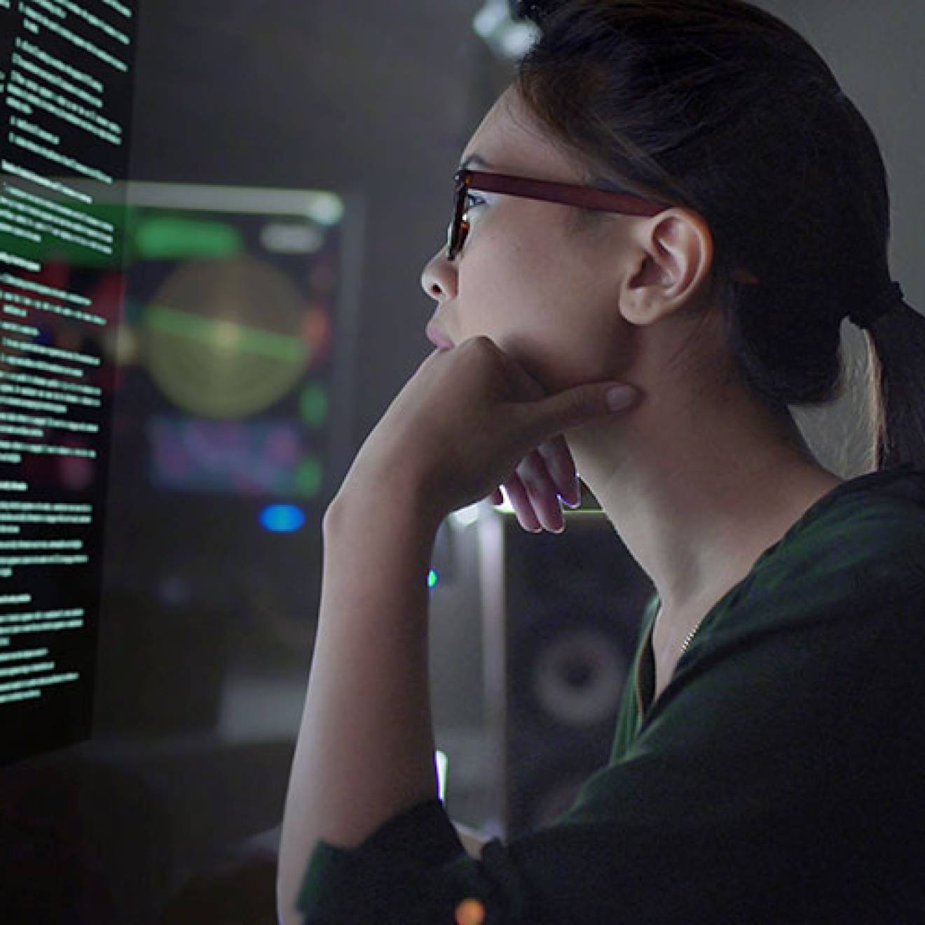 Young Asian woman looking at code on a screen in a dark room