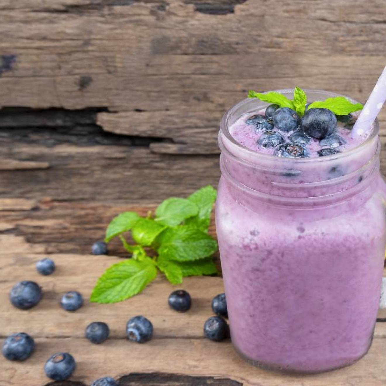 A purple smoothie with blueberries and a banana next to it on a table