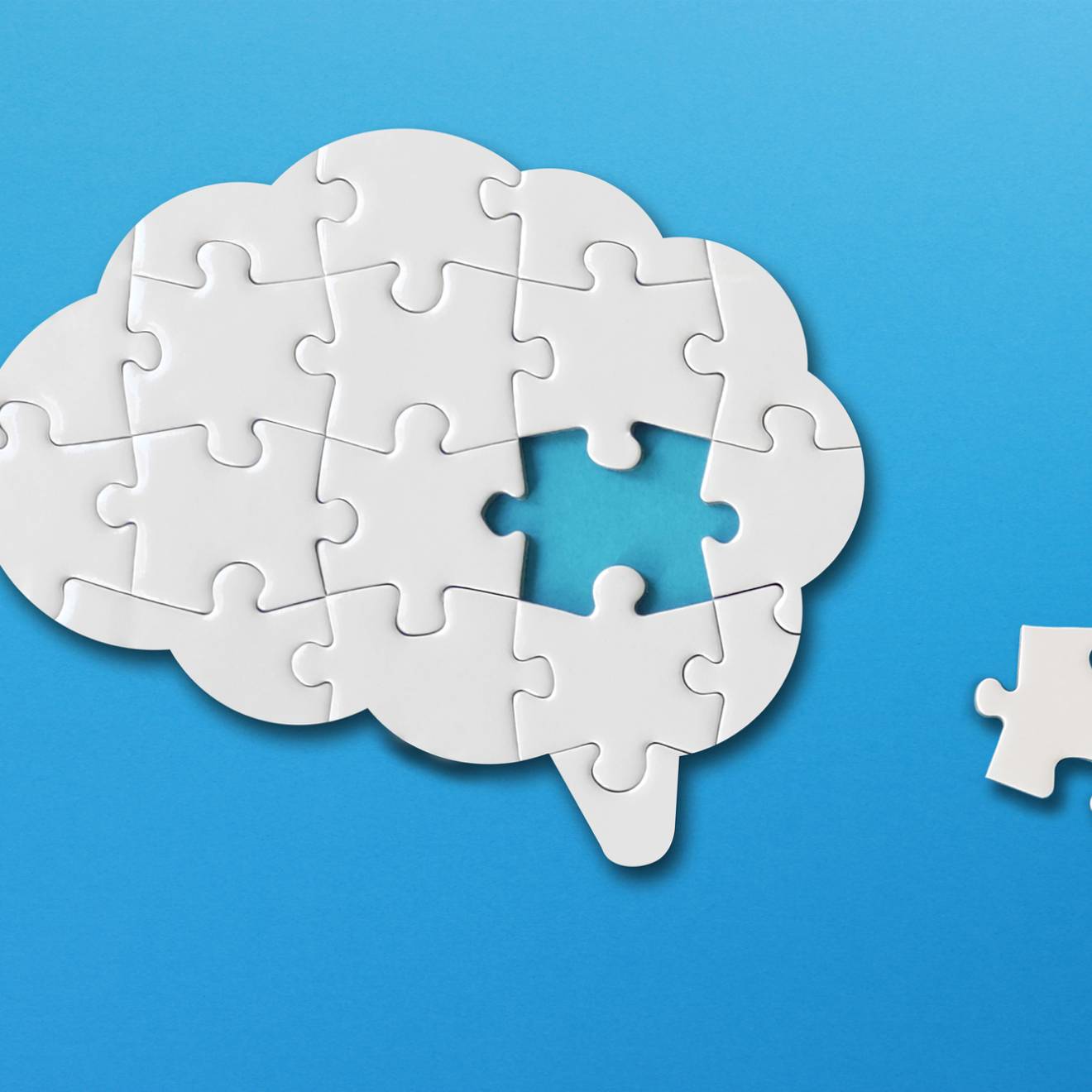A puzzle of a brain with one piece to the side; puzzle is white on a blue background