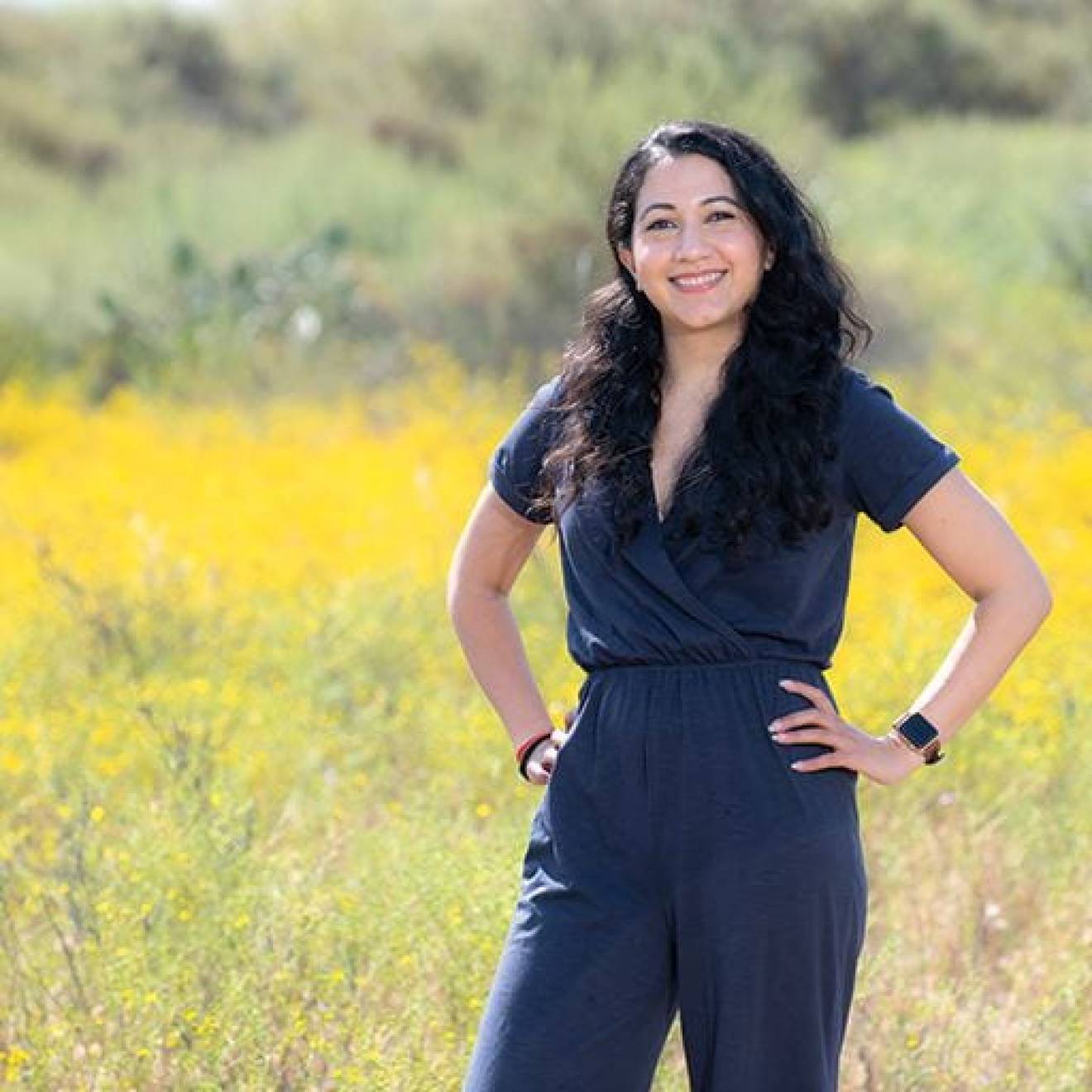 Woman with long dark hair, Shyla Raghav, standing in front of a yellow field of wildflowers