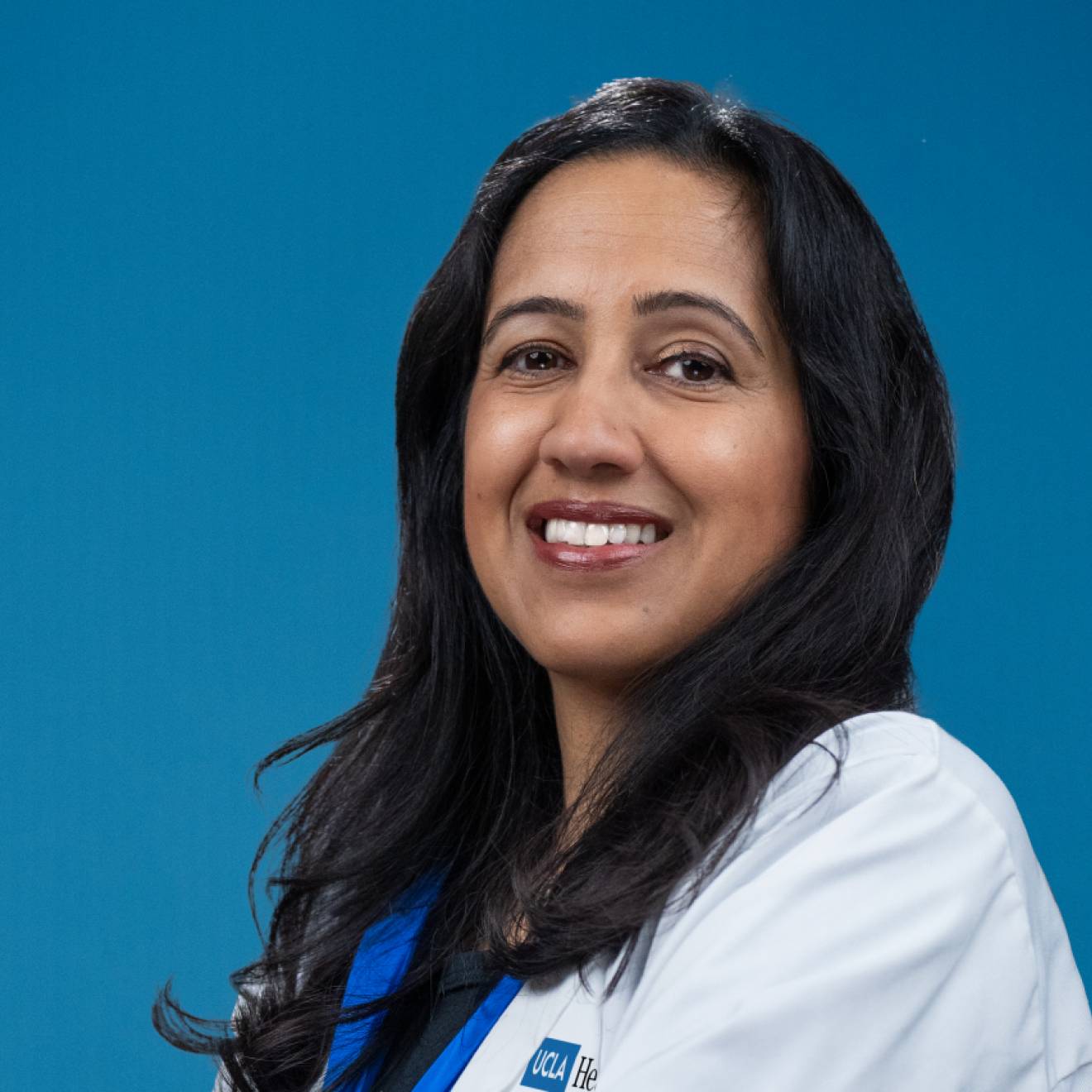 A portrait of a smiling woman with long hair in a white medical coat on a blue background
