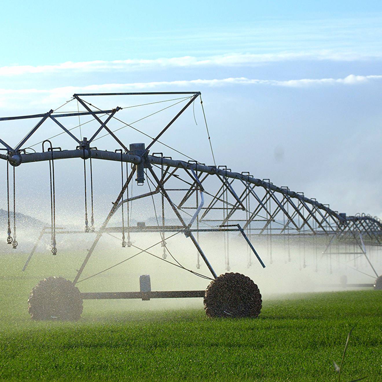 A spray irrigation system of metal irrigation equipment on a green field with mountains and clouds in the background