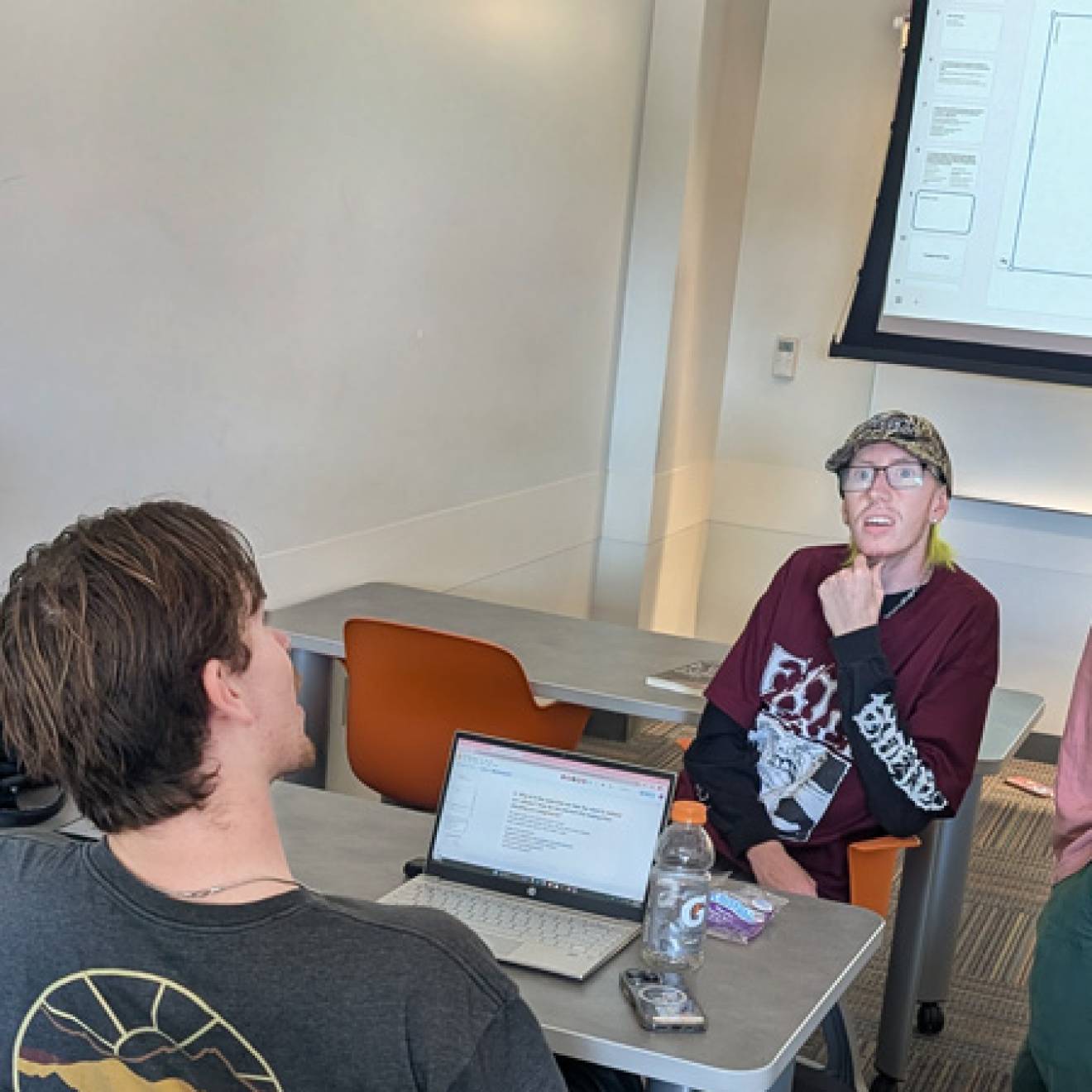 Three seated people talk to a standing professor in a classroom