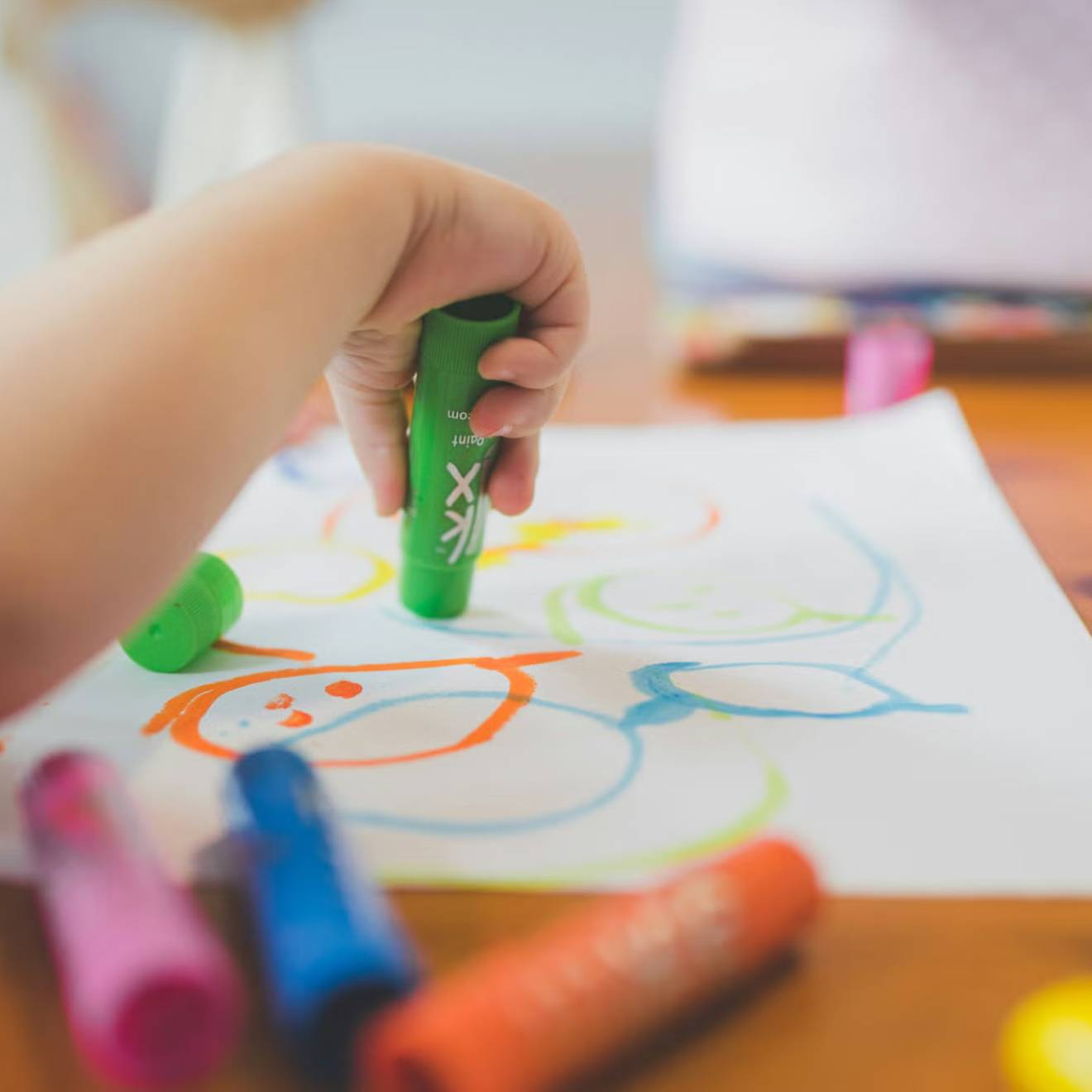 A child at a table draws on a piece of paper with crayons