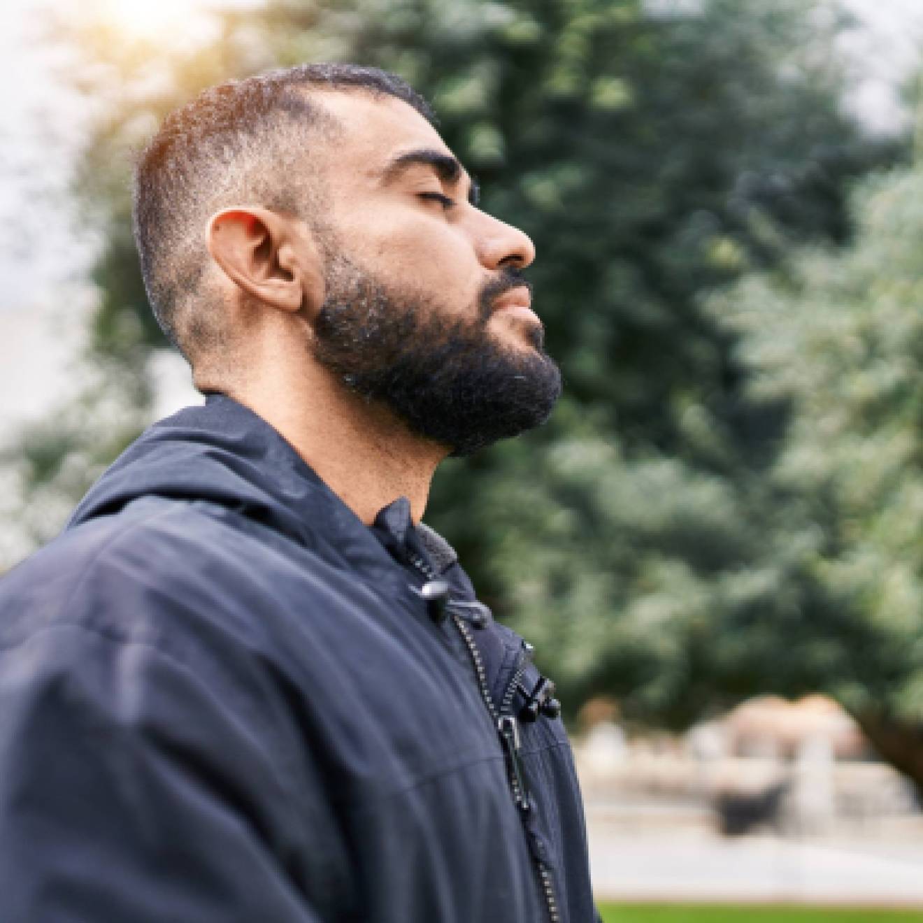 Young hispanic man with eyes closed taking a deep breath outside
