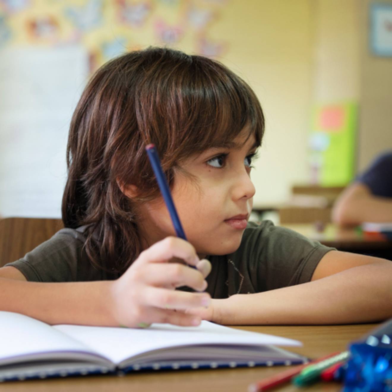 Boy looking up in a classroom, pencil in workbook