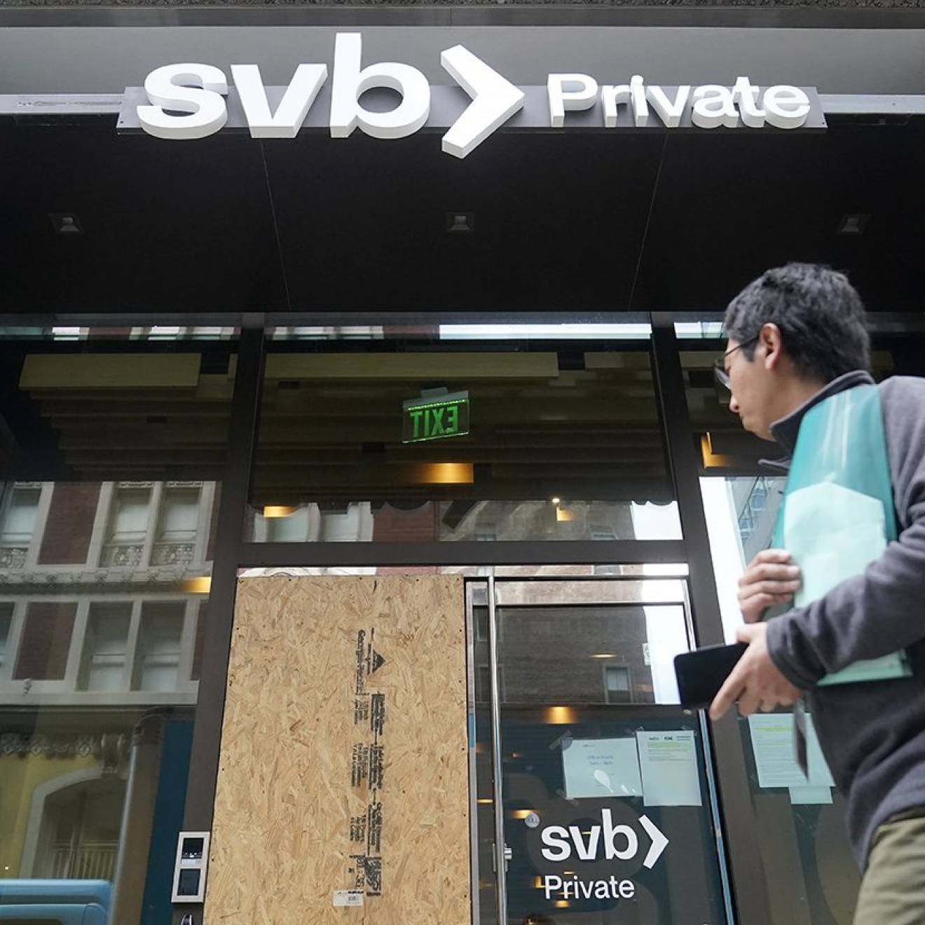 Someone walks by the SVB bank with one door boarded up