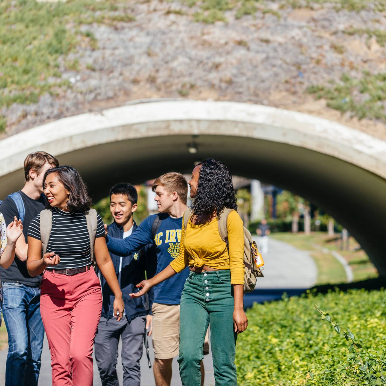 Diverse small group of happy students walking away from an arch on UC Irvine campus