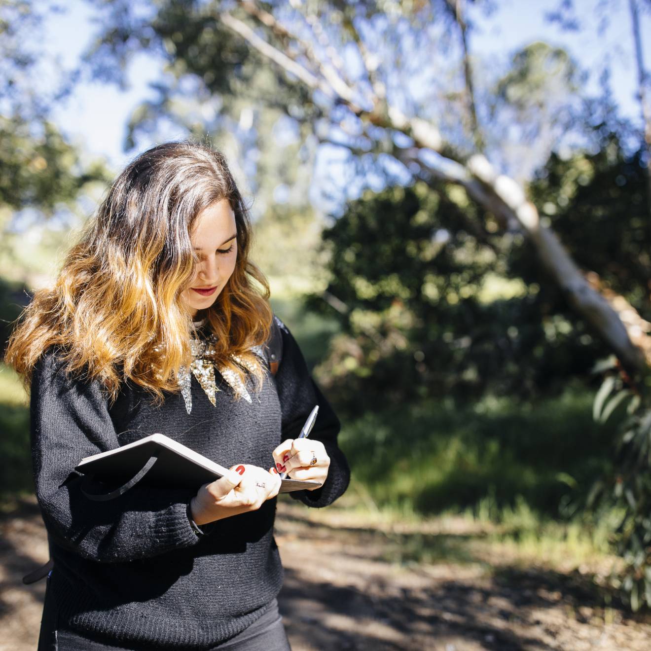 Young woman writing in notebook walking through woods