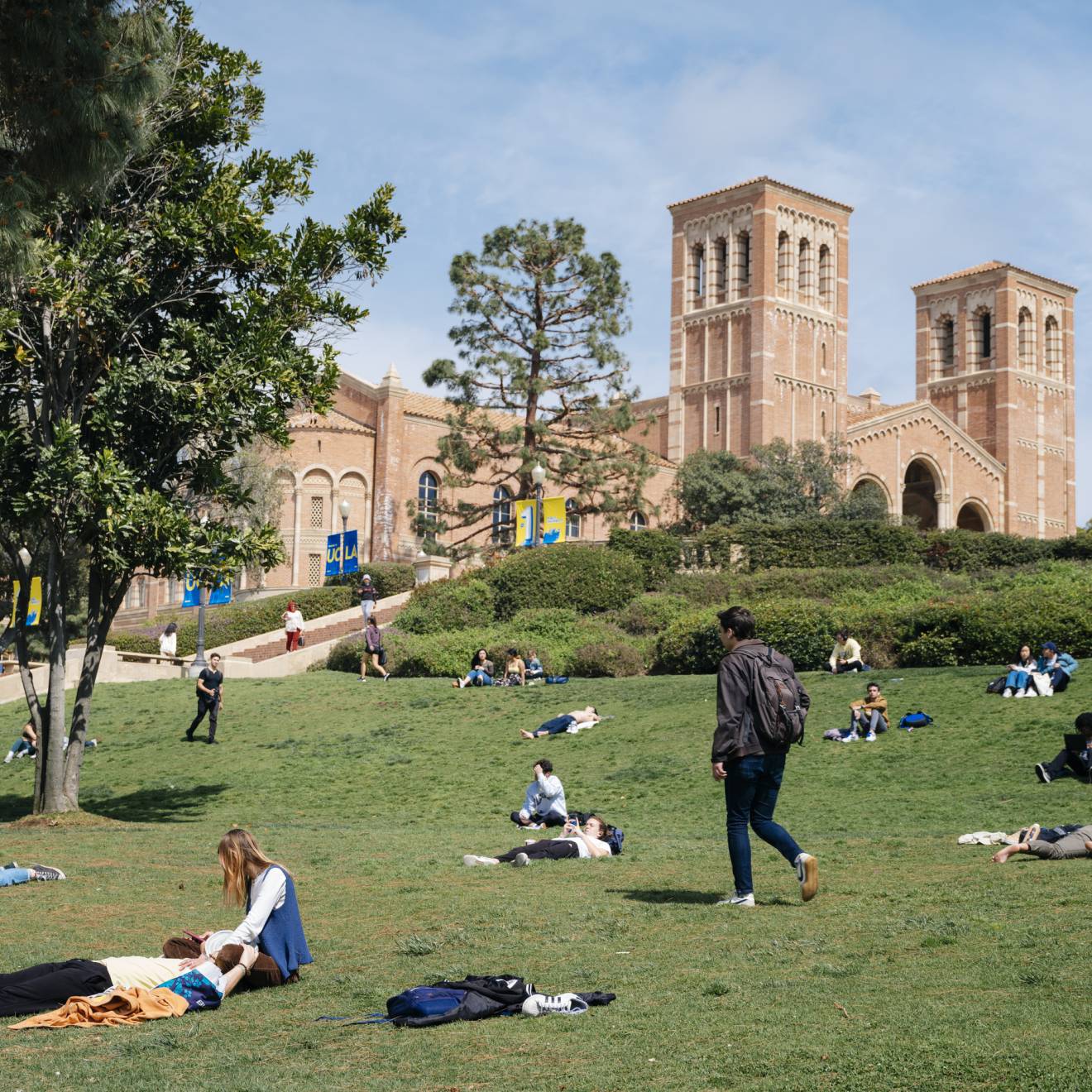 Students lounge and walk across the green on a sunny day at the UCLA campus; Royce Hall in the background