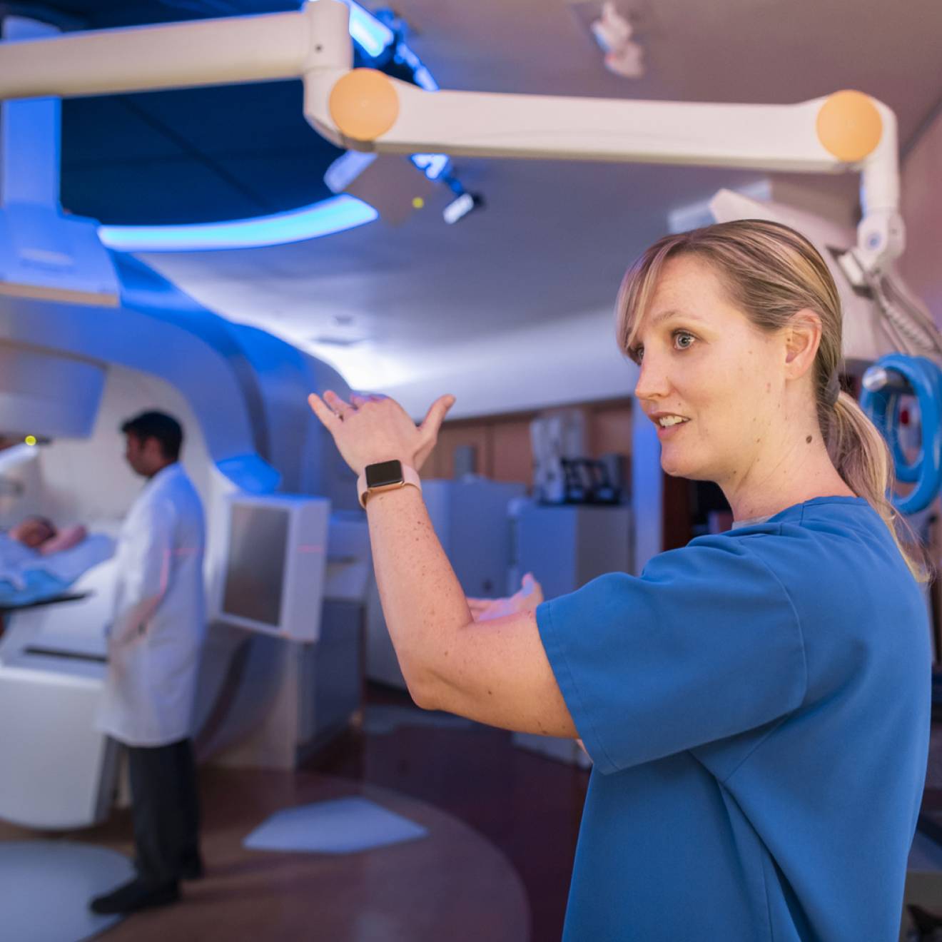 A nurse explaining something while a scan happens behind, doctor standing by