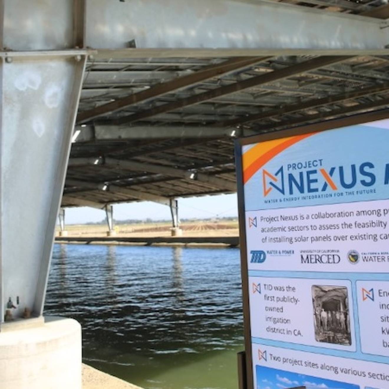 A water canal covered by a solar panel canopy, with a sign for the Nexus project pilot