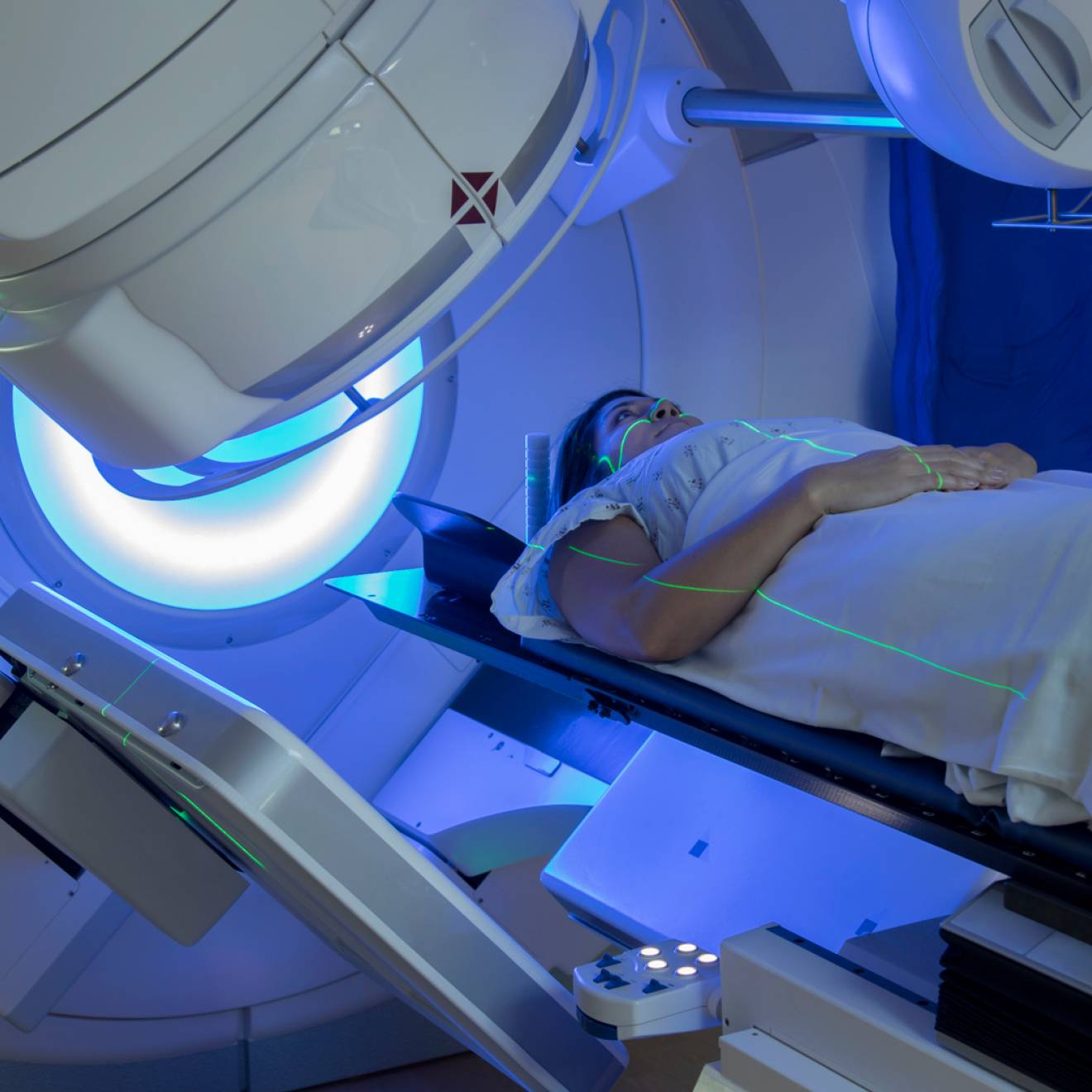 Woman receiving radiation therapy treatments for breast cancer under a machine with green lines of light on her face and body