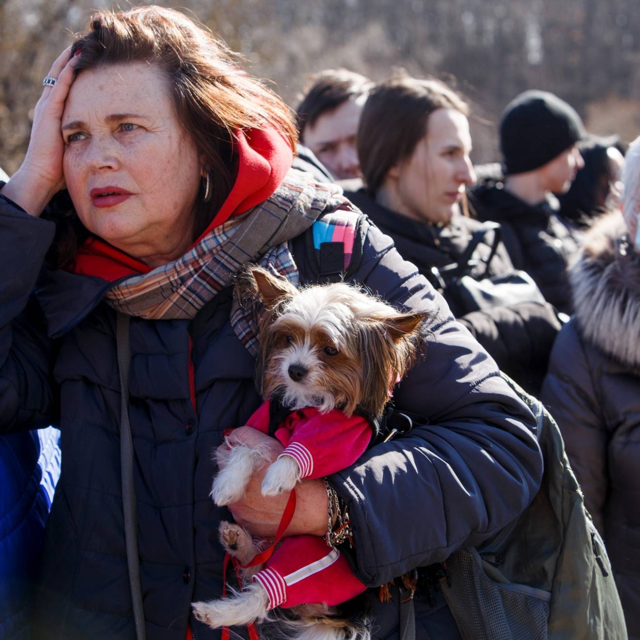 A group of Ukrainian refugees standing outside in winter coats, a middle-aged woman holding a small dog in front