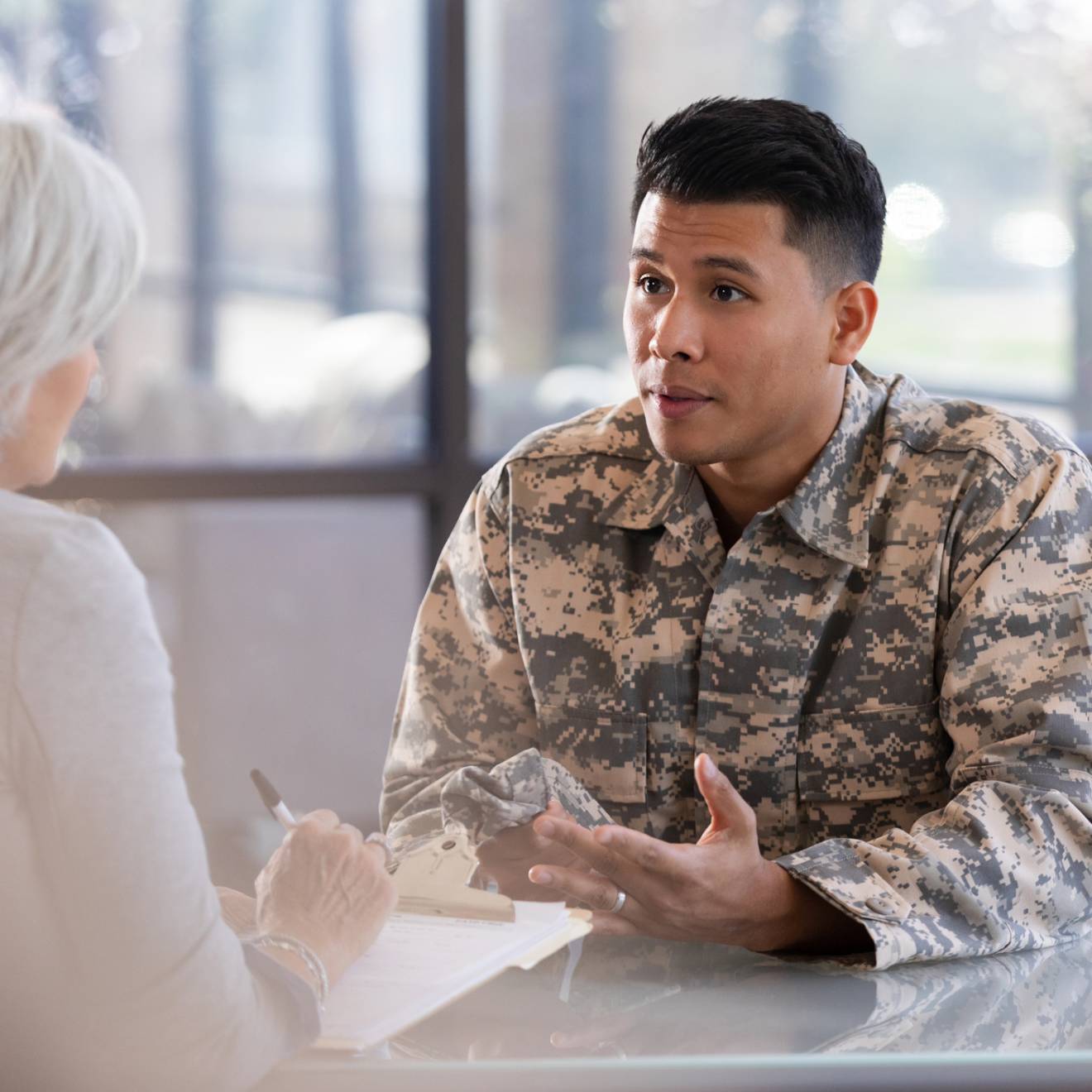 A soldier in uniform consults with a healthcare worker, discussing personal matters in a professional office