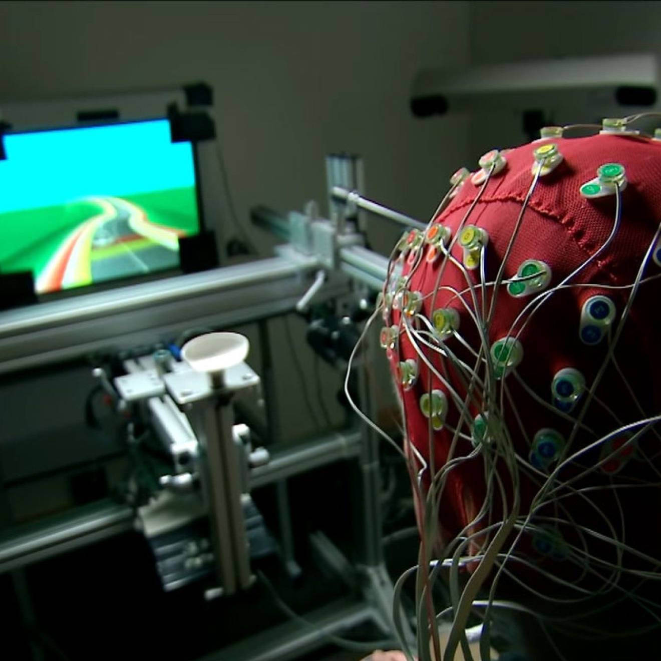 Someone with a cap for monitoring brain activity on their head plays a video game