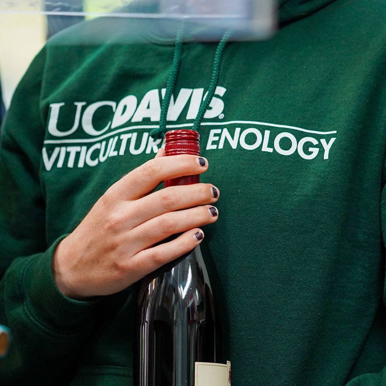 A woman in a green UC Davis viticulture sweatshirt holds a wine bottle